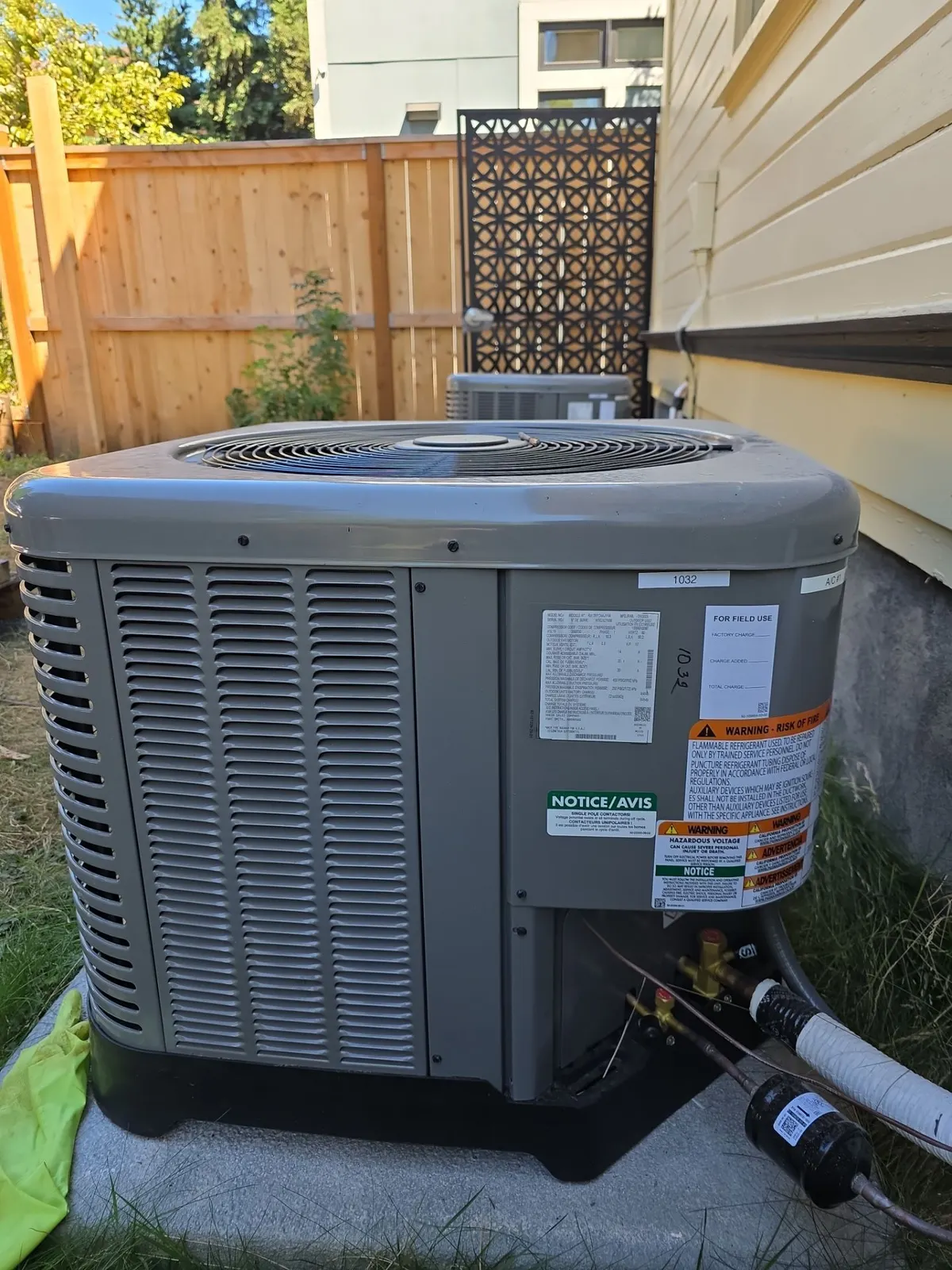 New gray AC condenser on a pad with a filter drier and insulated line set beside a wood fence