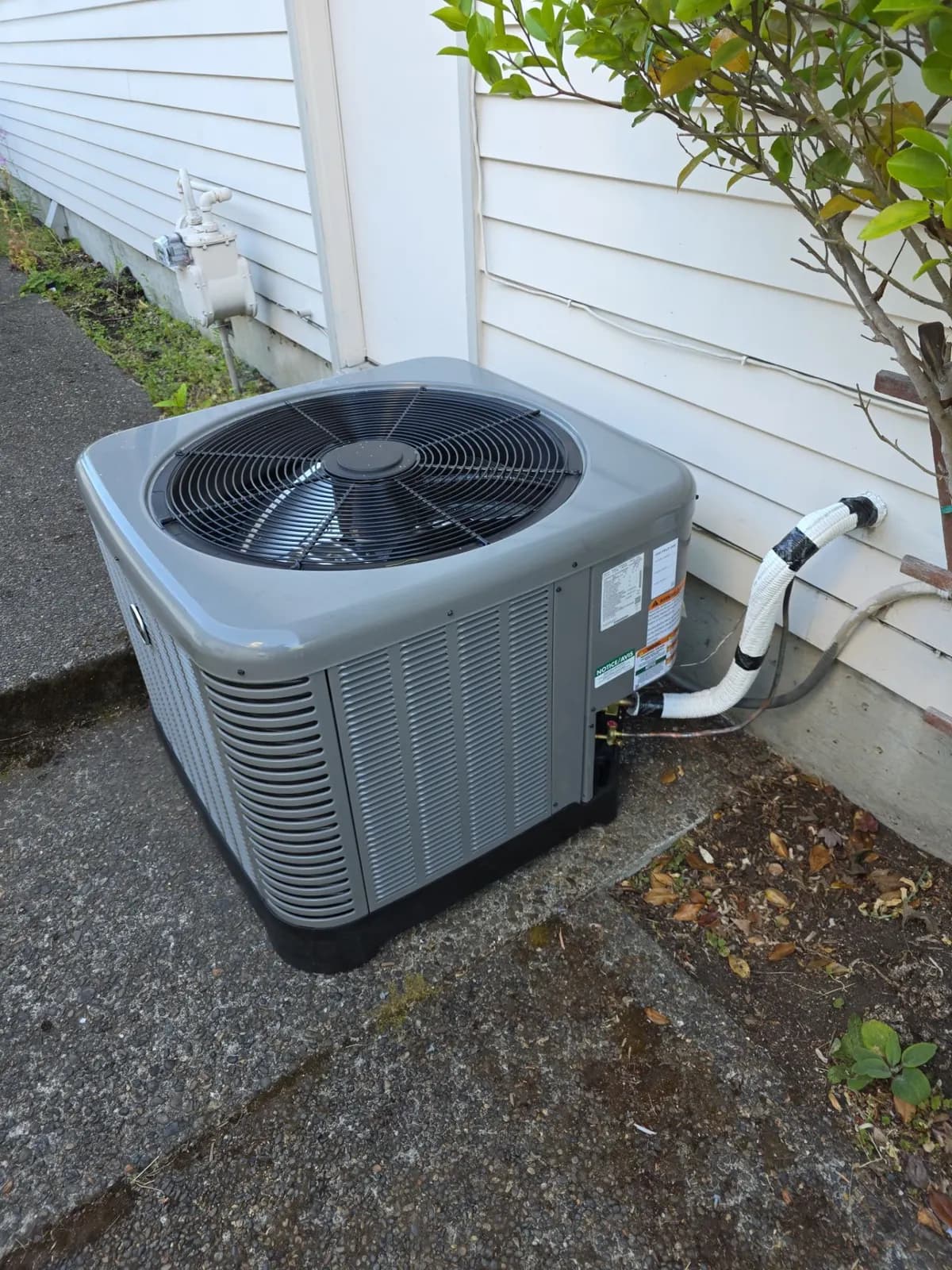 New gray air conditioner condenser in a narrow side yard beside white siding
