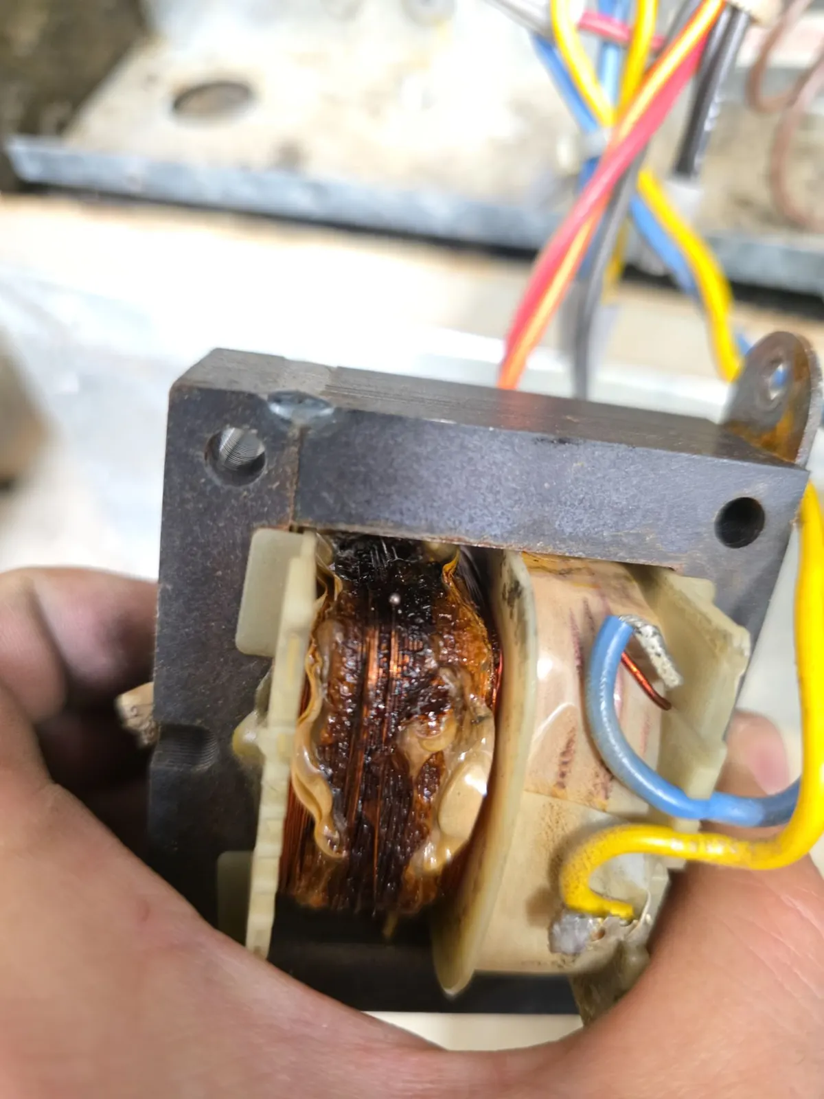 Hand holding a failed control transformer with burned, melted windings