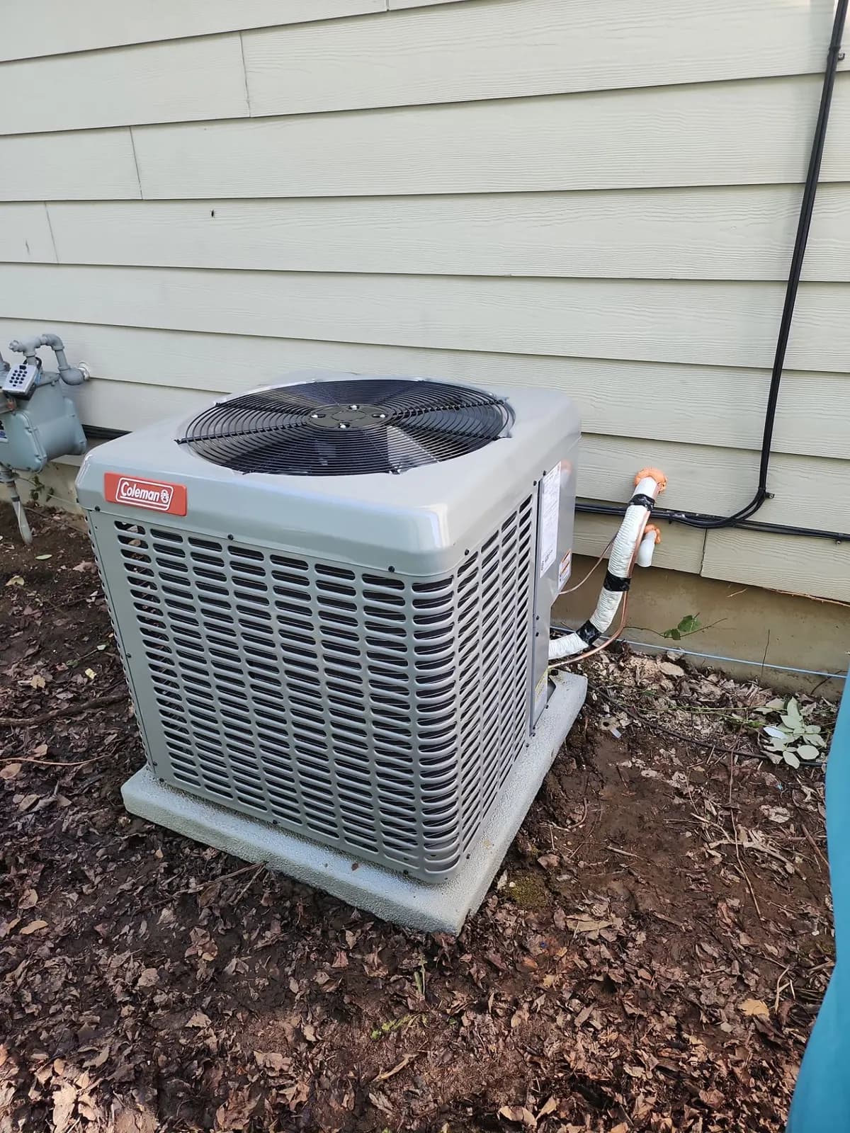 New Coleman air conditioner condenser on a pad beside tan siding