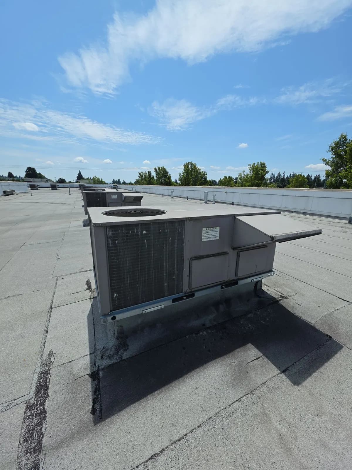 Row of packaged rooftop HVAC units on a large flat commercial roof under blue sky