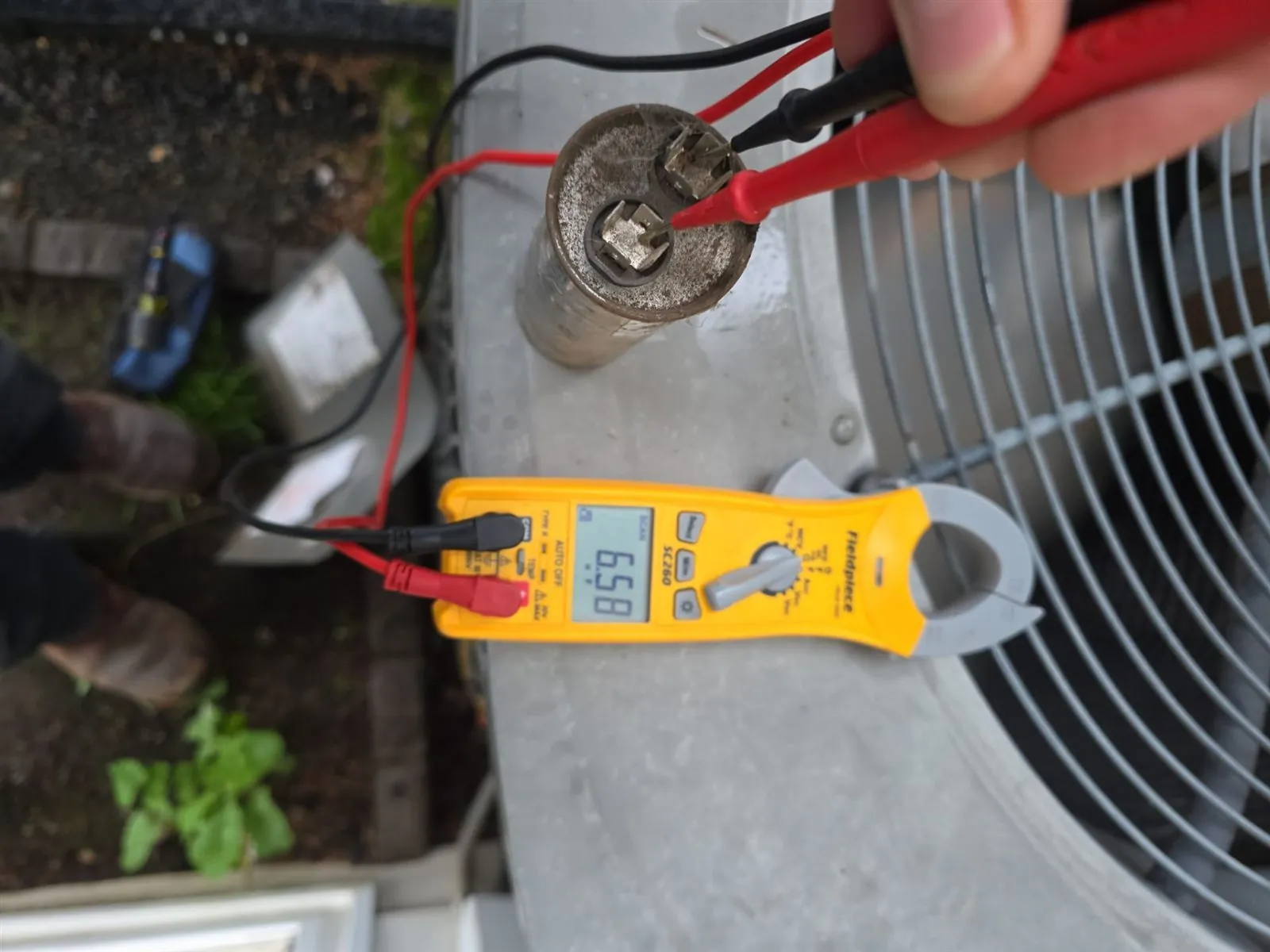 Technician testing an AC condenser capacitor with a clamp meter