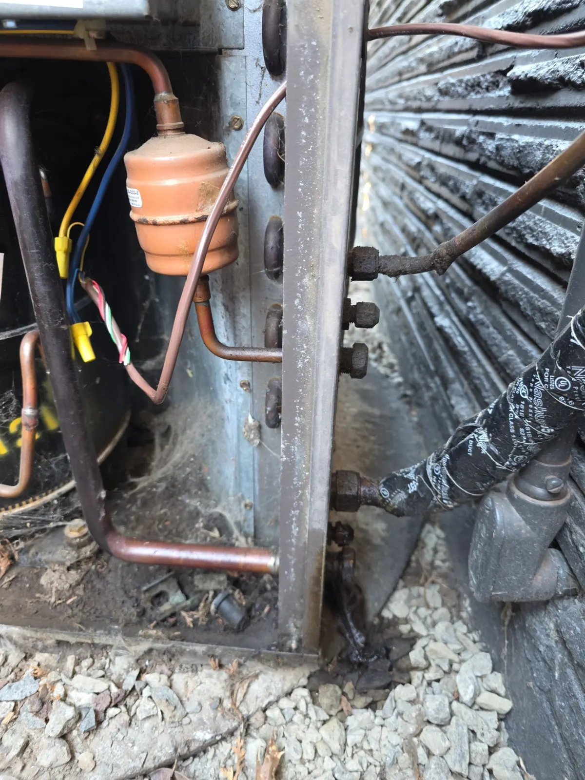 Inside an older condenser showing rusted service valve fittings, a filter drier and oily residue