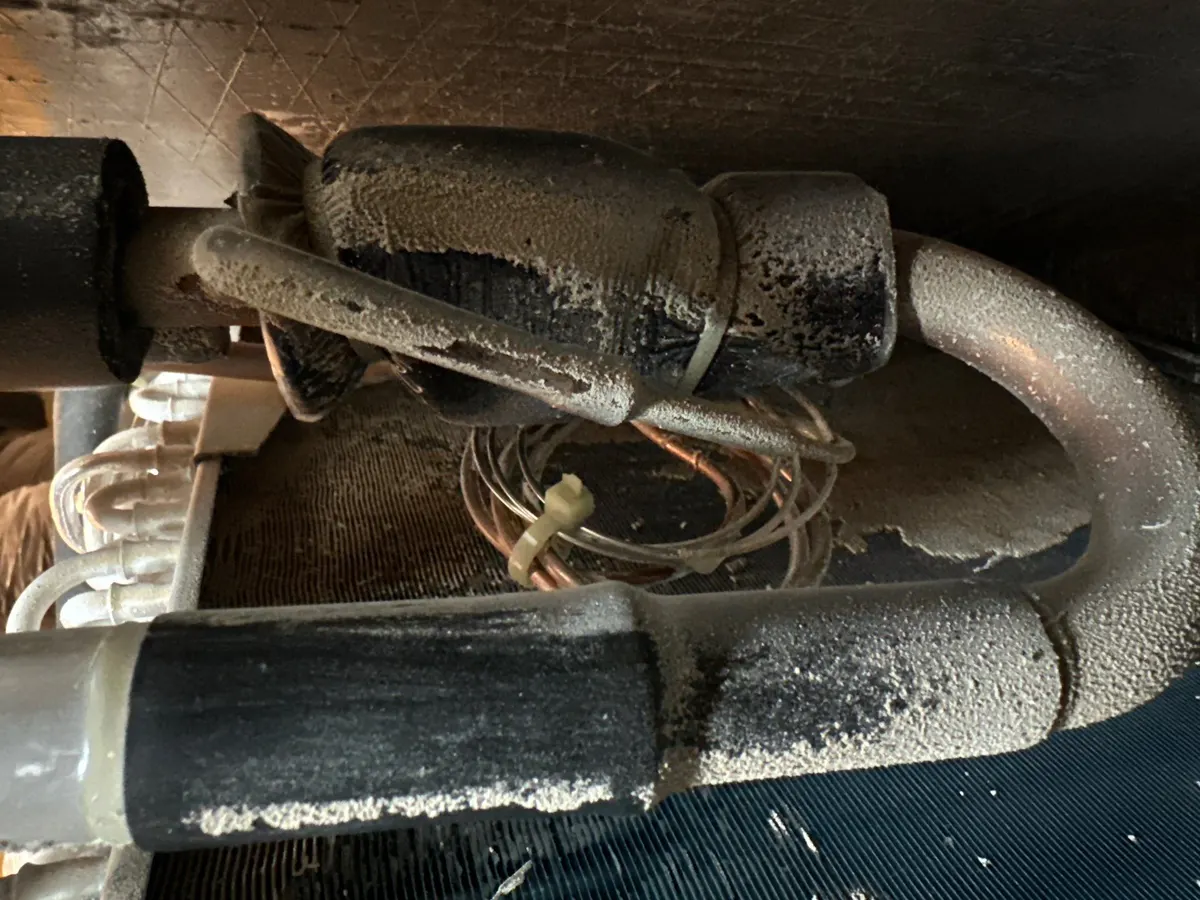 Indoor evaporator coil piping and expansion valve covered in white corrosion and dirt