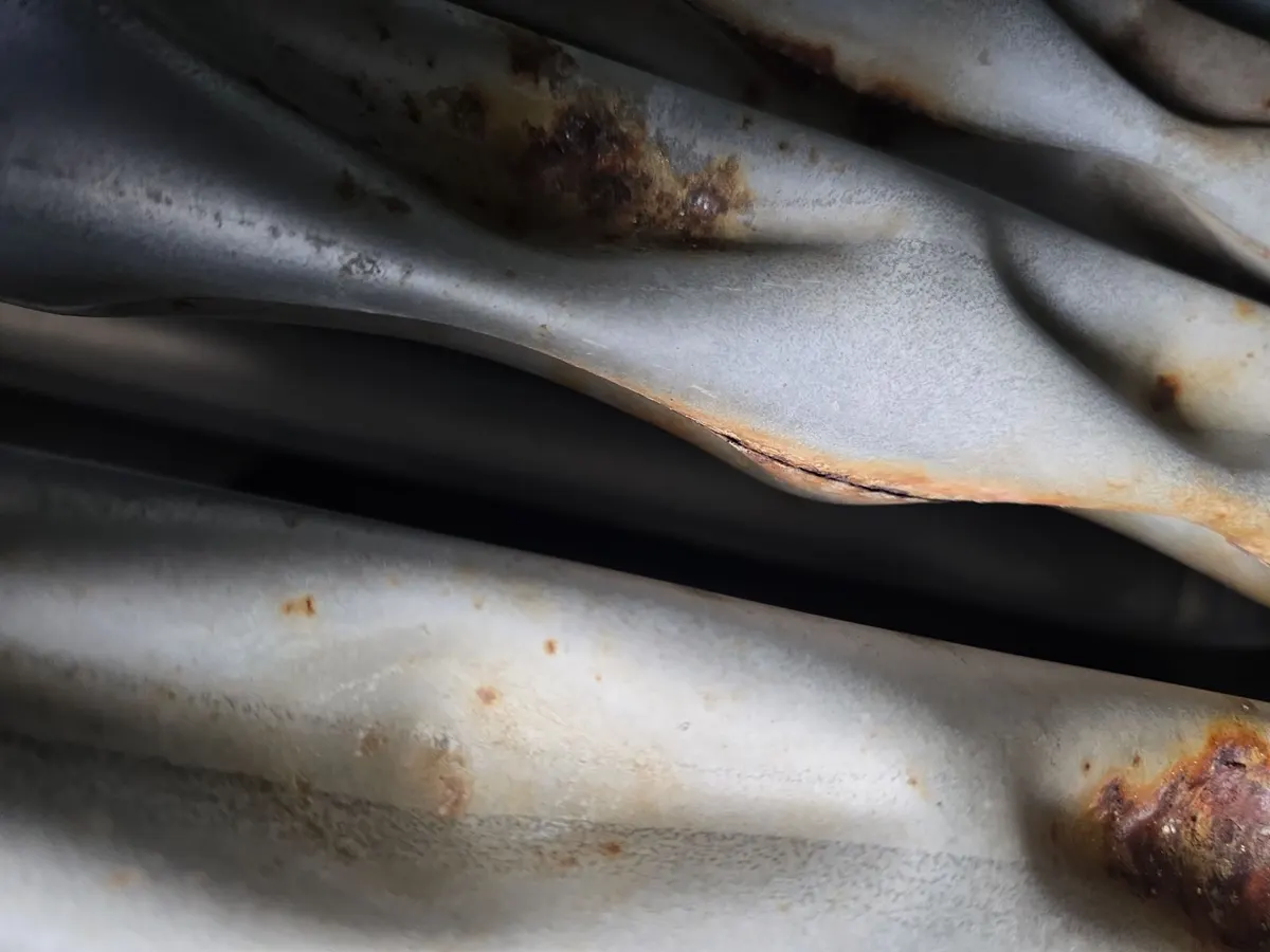 Close-up of rooftop unit heat exchanger tubes with rust and a crack along a seam