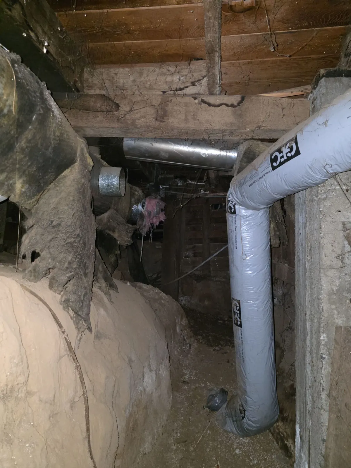 Crawlspace with old torn duct insulation beside a new insulated flex duct run