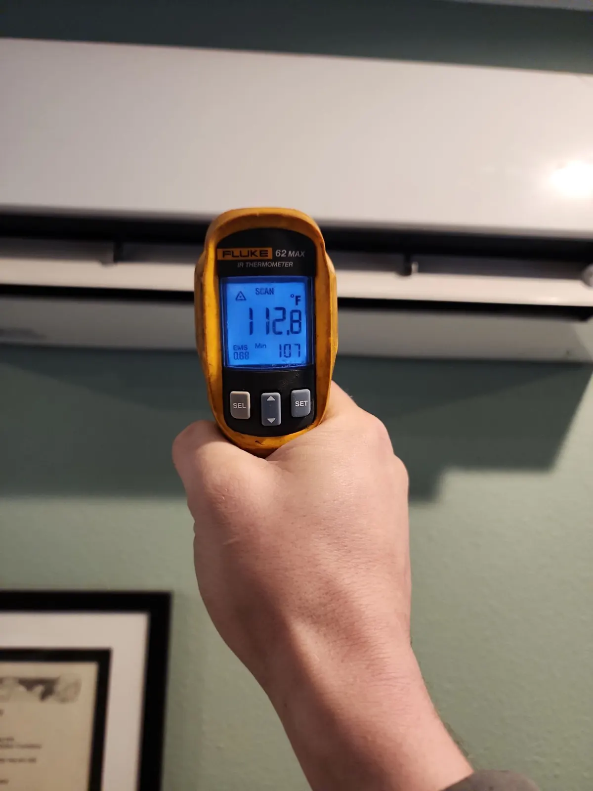 Hand holding an infrared thermometer reading 112.8 degrees at a ductless head's vent