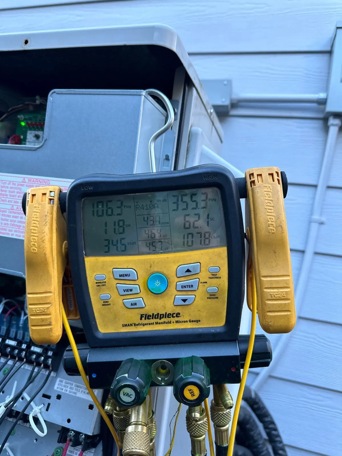 Digital refrigerant gauge manifold hanging on an open ductless heat pump outdoor unit