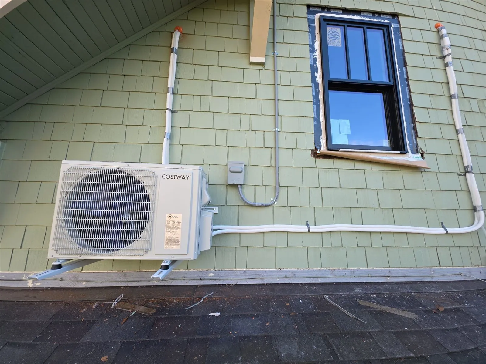 Mini split outdoor unit mounted on a green shingled wall with white line set covers