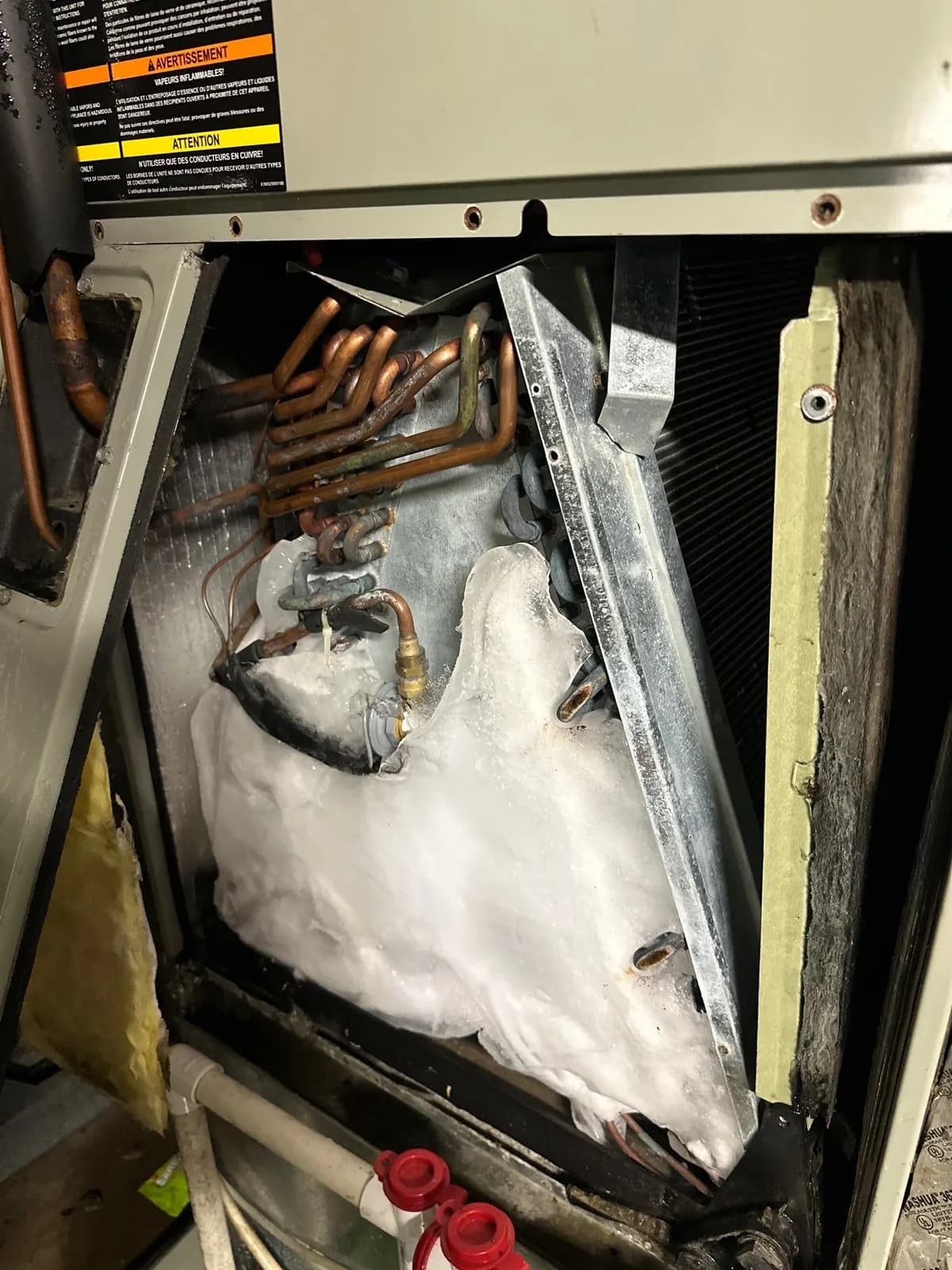 Air handler with the panel off showing the evaporator coil and copper piping covered in thick ice