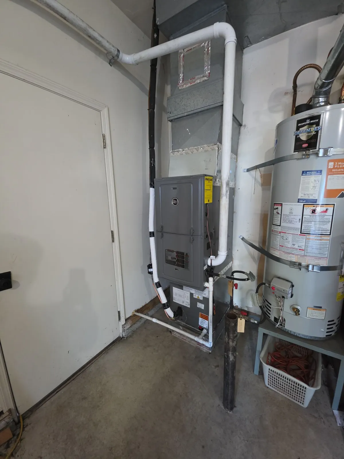 New furnace with an evaporator coil and PVC venting in a garage closet beside a gas water heater