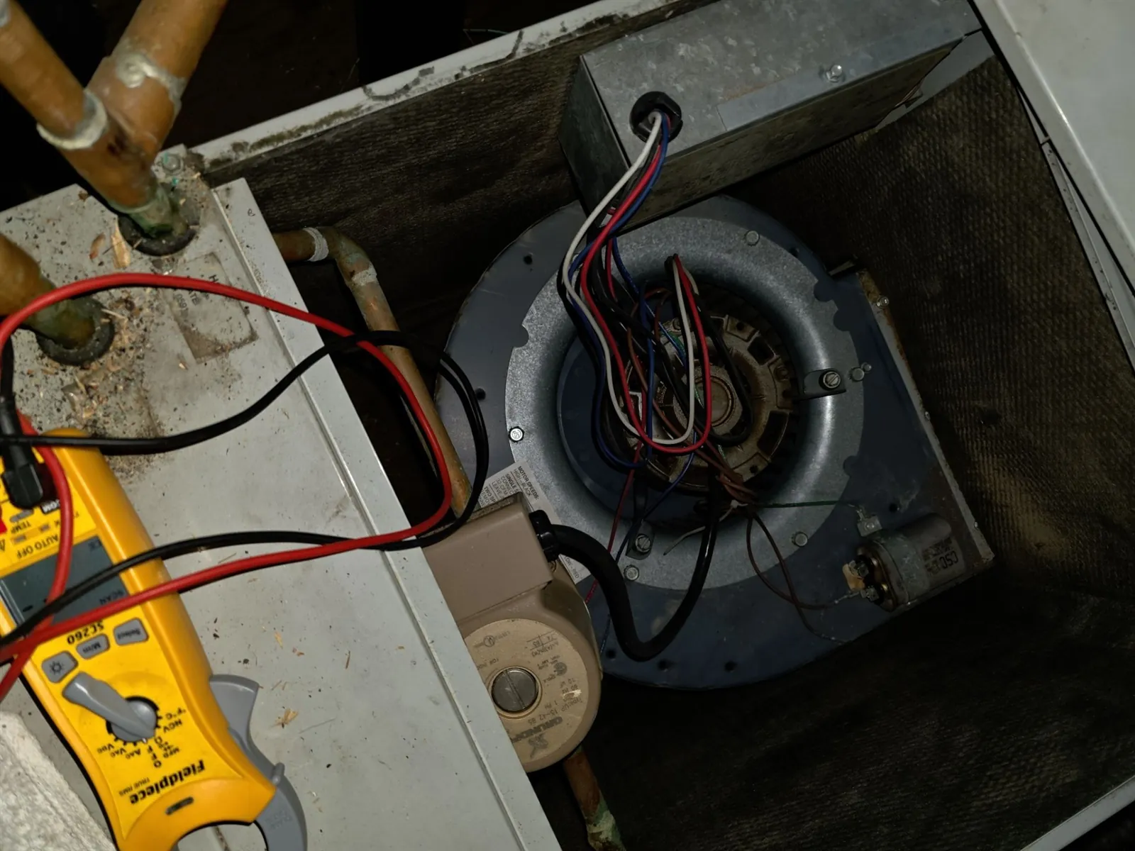 Clamp meter testing the blower motor inside an open furnace cabinet