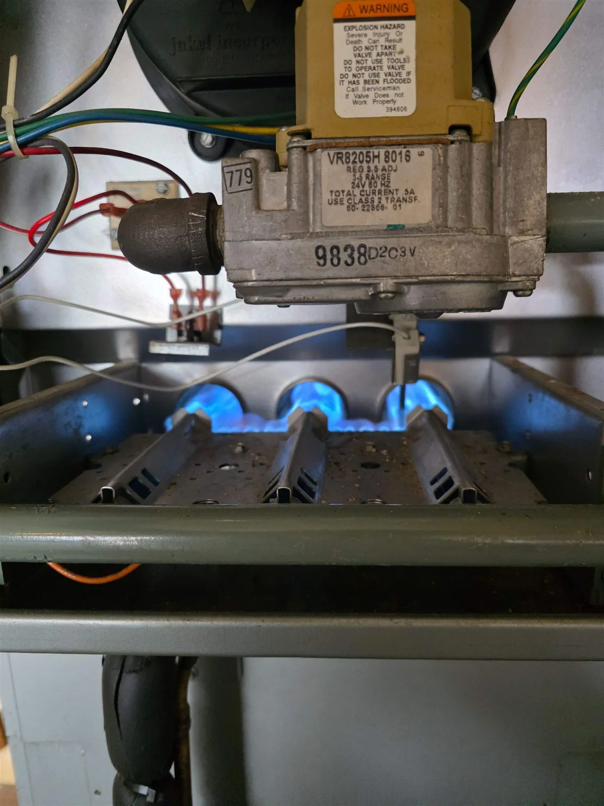 Blue burner flames and gas valve inside an open gas furnace during a tune-up