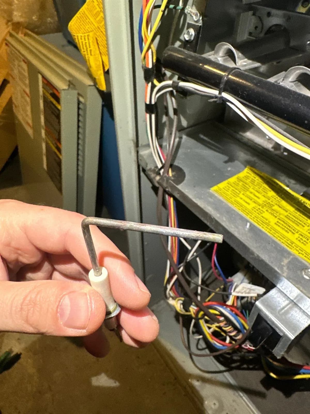 Technician holding a furnace flame sensor in front of an open gas furnace