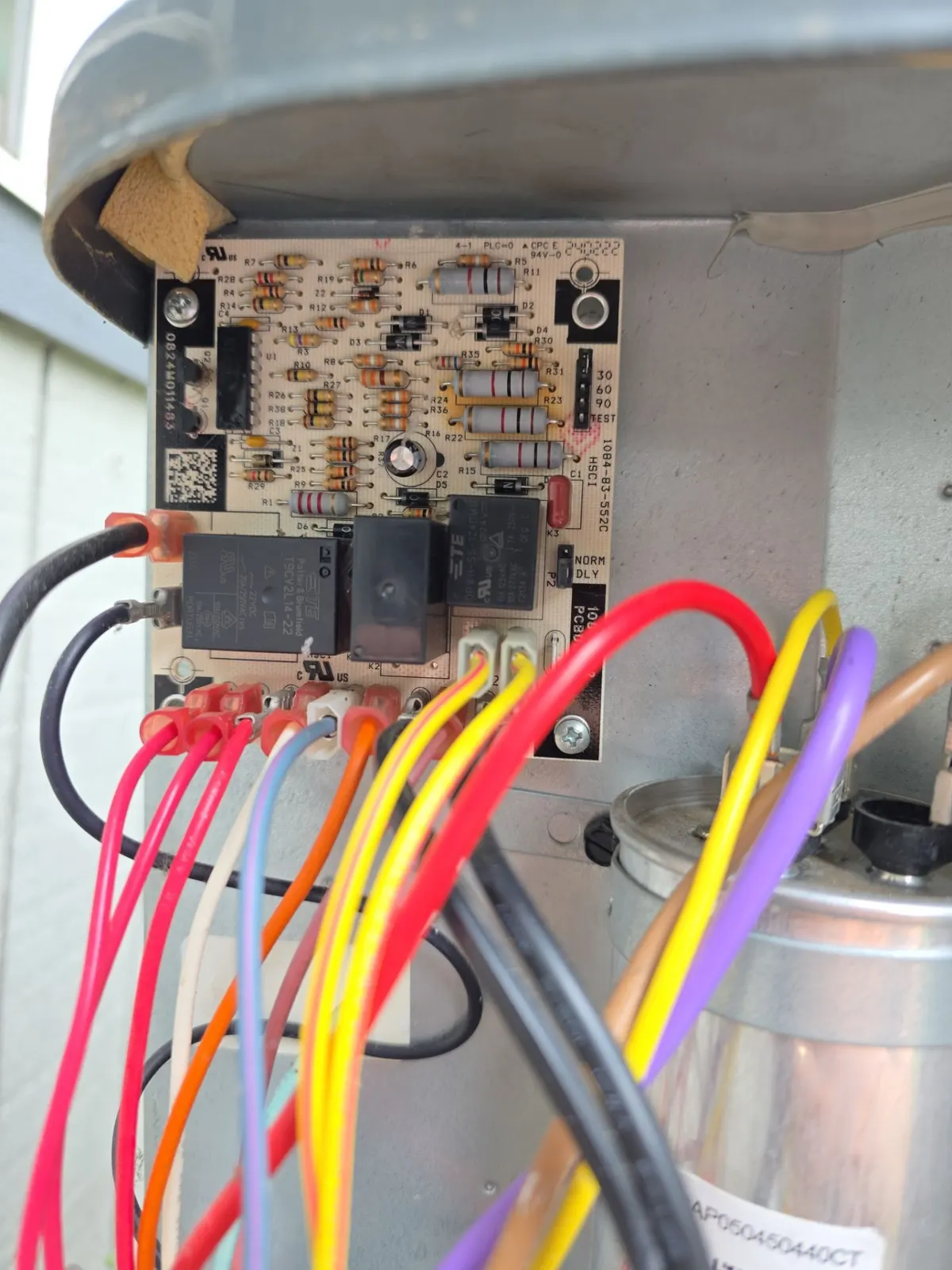 Heat pump defrost control board with relays and colored wiring above the run capacitor