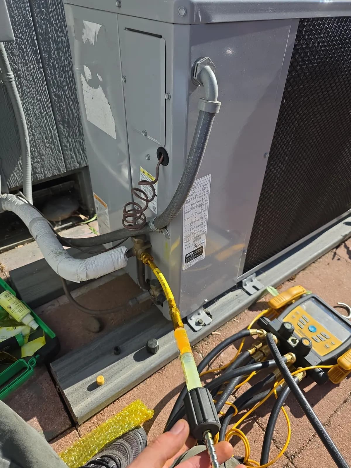 Technician connecting a leak-detection dye injector to the service valve of an outdoor unit