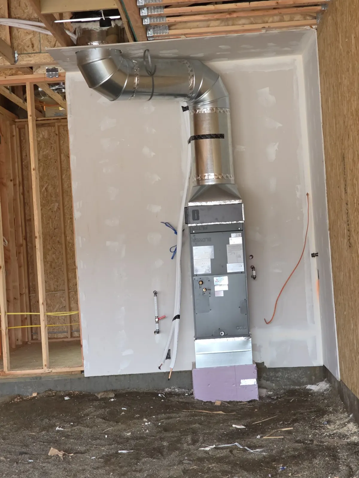 Air handler in a framed room with round sheet metal duct running into the ceiling