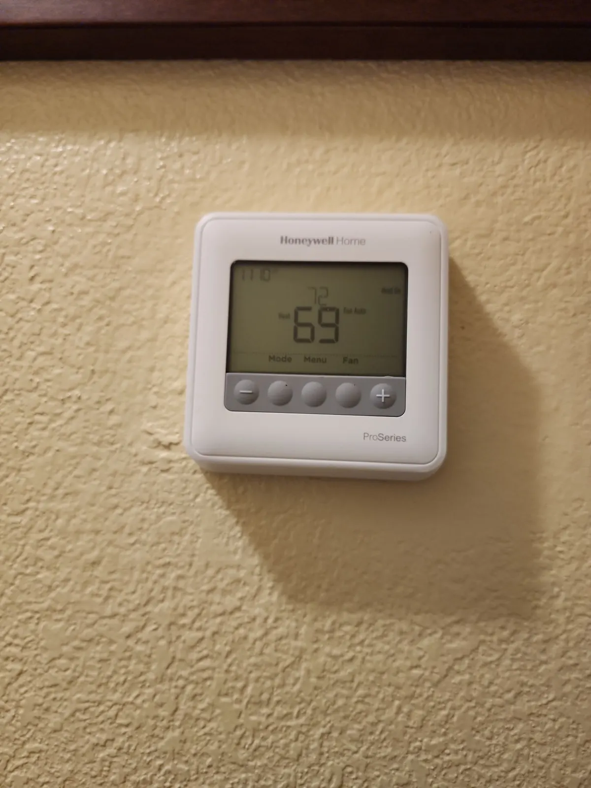 White programmable thermostat on a beige wall showing 69 degrees