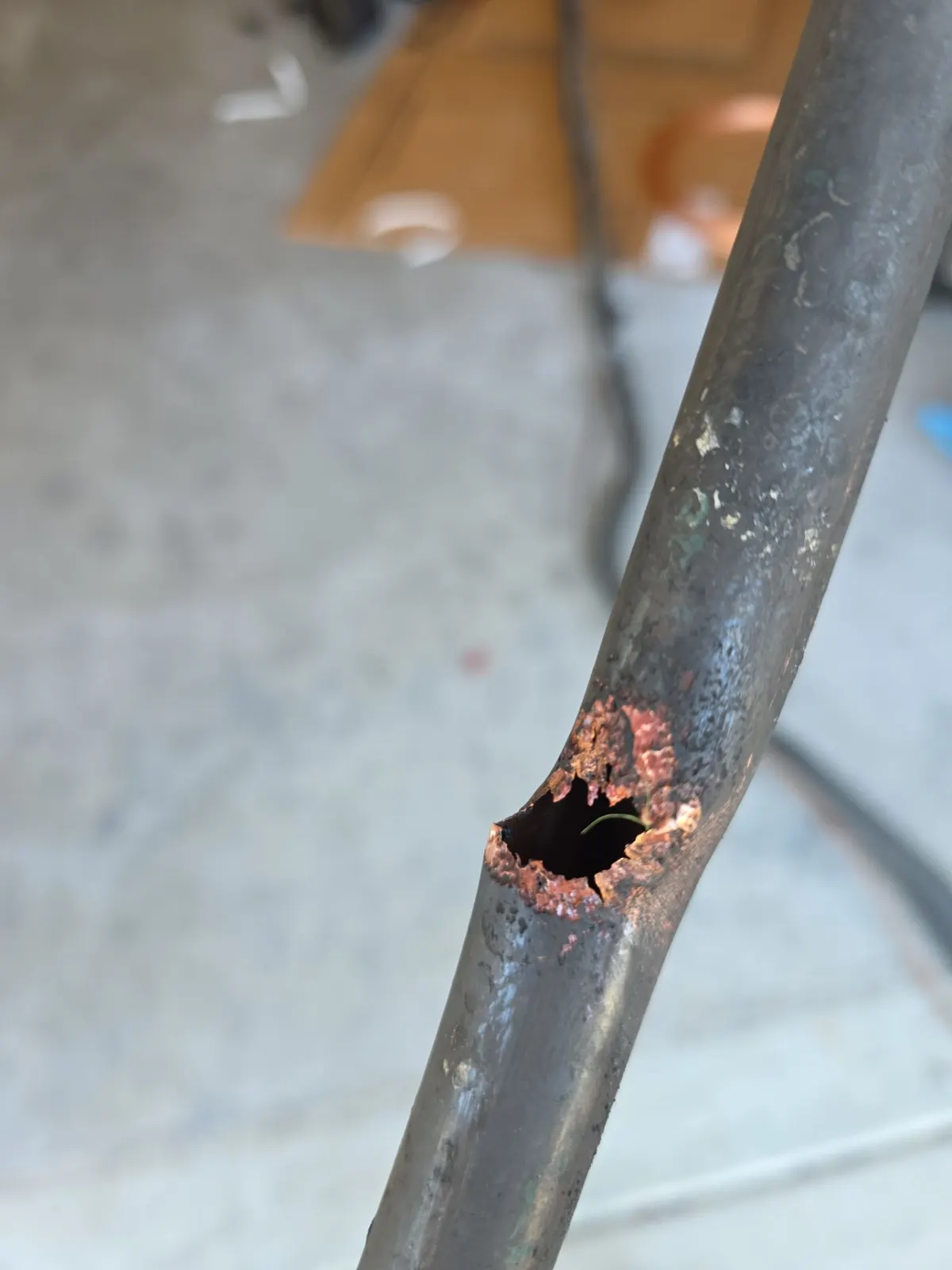 Close-up of a corroded copper refrigerant line with a hole rusted through it