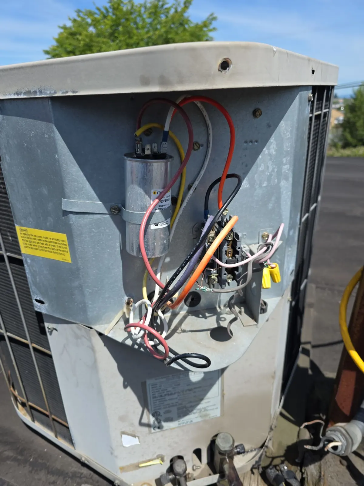 Rooftop condenser with the service panel off showing the capacitor, contactor and wiring