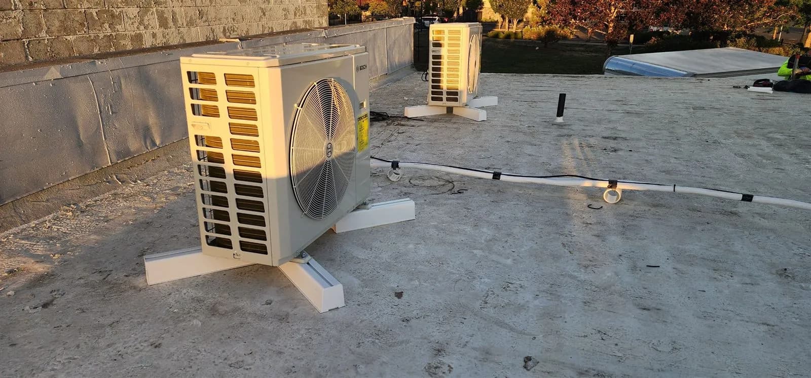 Two mini split condensers on roof stands with line sets run across a commercial roof