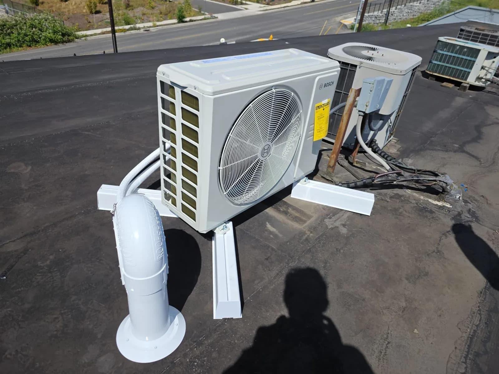 Mini split condenser on a flat roof stand with a line set roof penetration cover