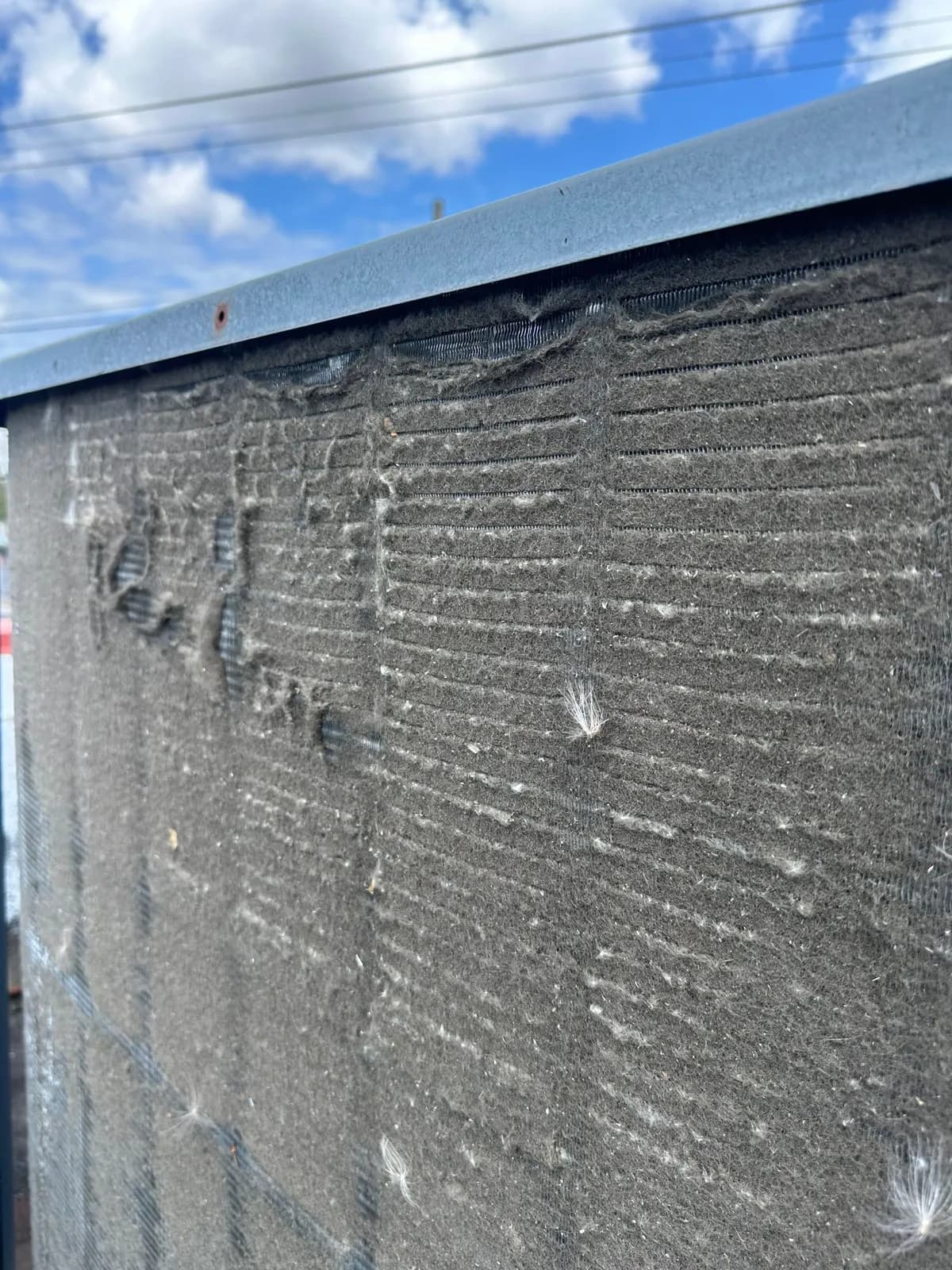 Rooftop unit condenser coil matted with lint and cottonwood fluff under a blue sky
