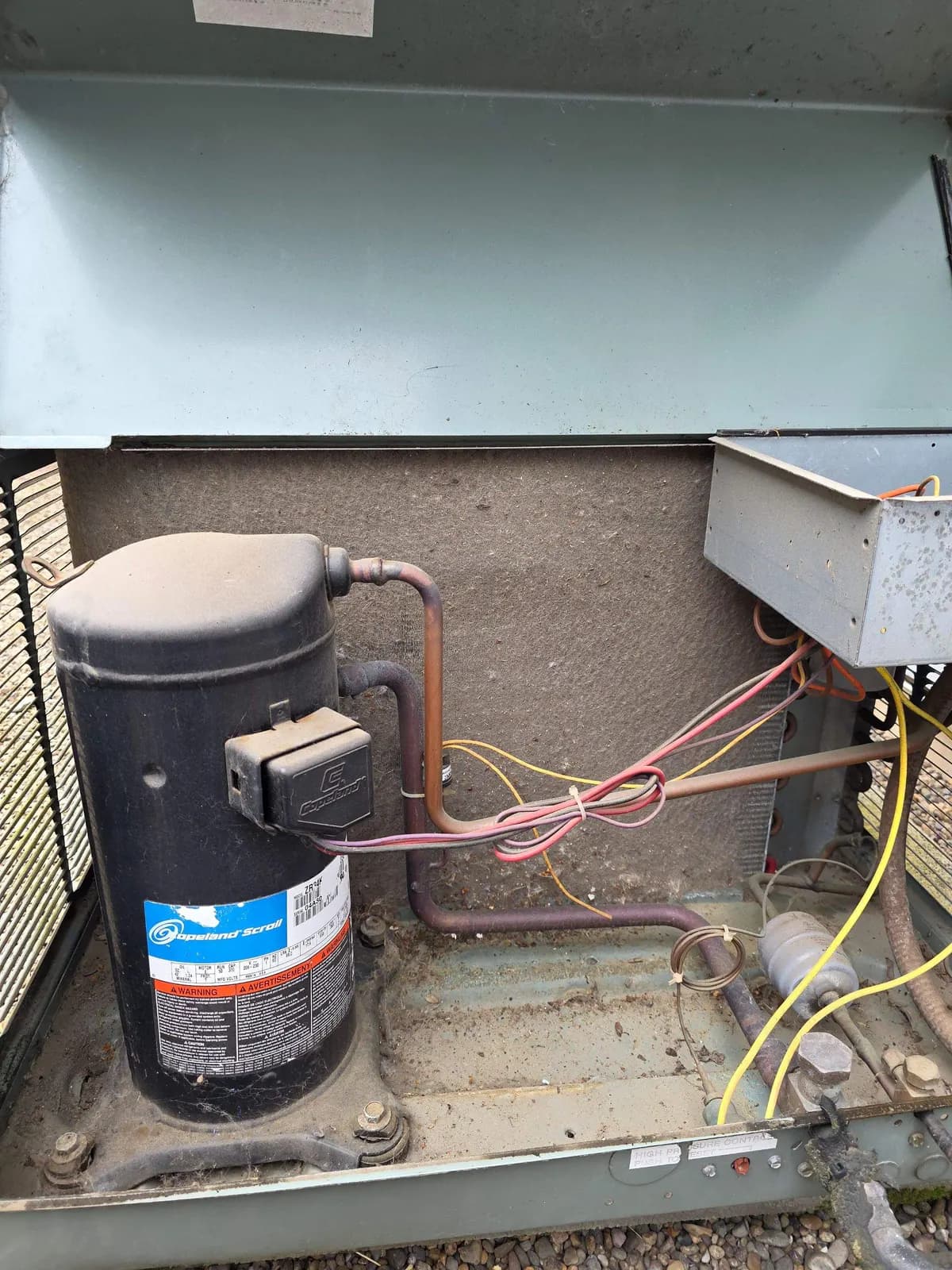 Open packaged rooftop unit showing a scroll compressor, wiring and filter drier