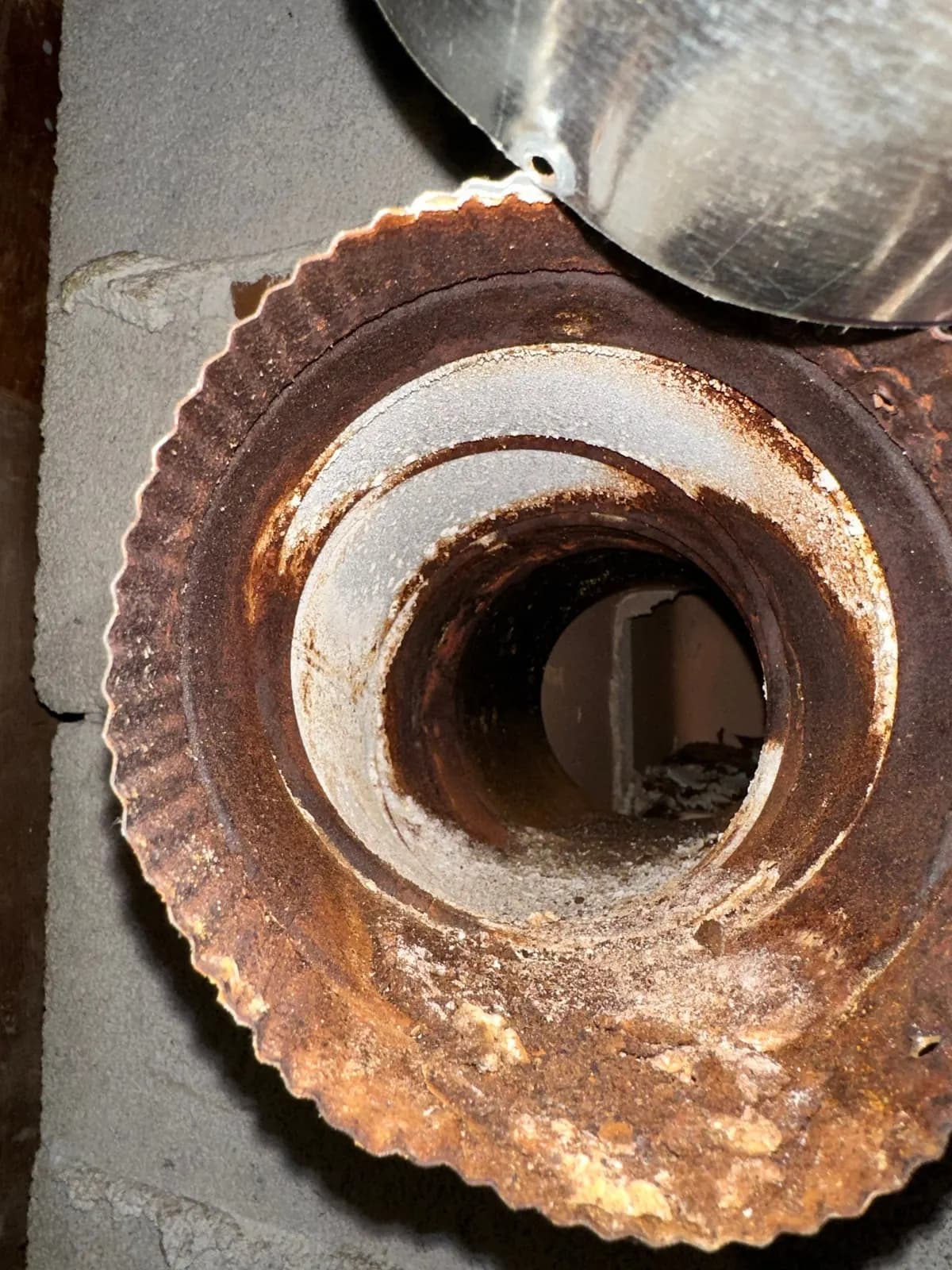 Heavily rusted flue pipe collar where it enters a block chimney