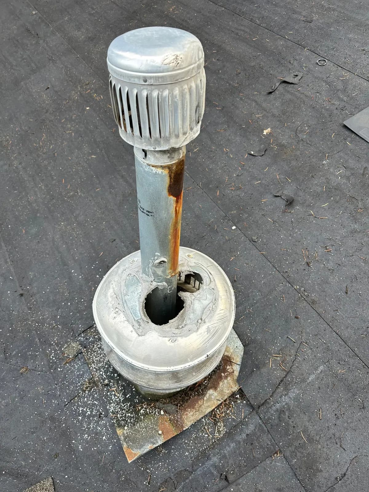 Gas vent pipe on a flat roof with a rust streak and a torn storm collar