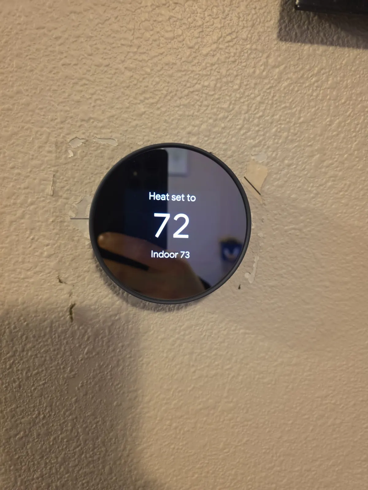 Round smart thermostat on a wall showing heat set to 72 and indoor temperature 73