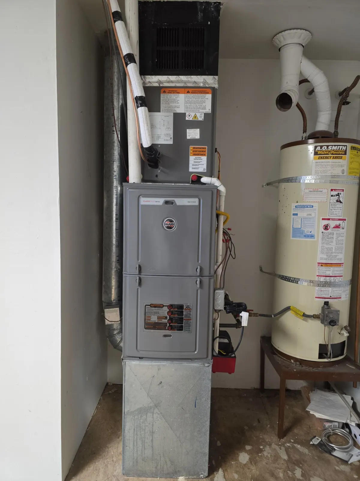 Gas furnace with an evaporator coil on top and PVC venting in a utility closet beside a water heater