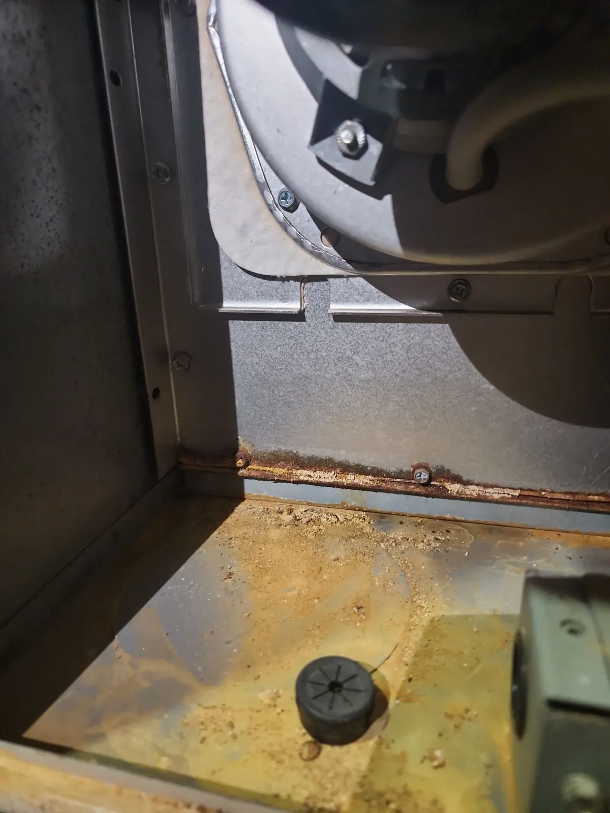 Rust and water staining across the floor of a furnace blower compartment