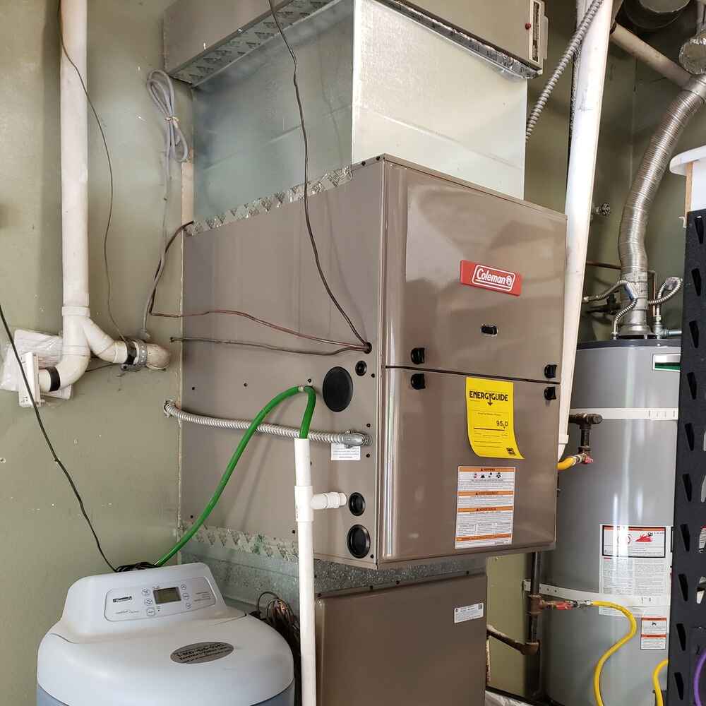 Furnace tune-up performed on a Coleman unit in a residential utility room, including inspection of duct connections, wiring, and drainage lines.
