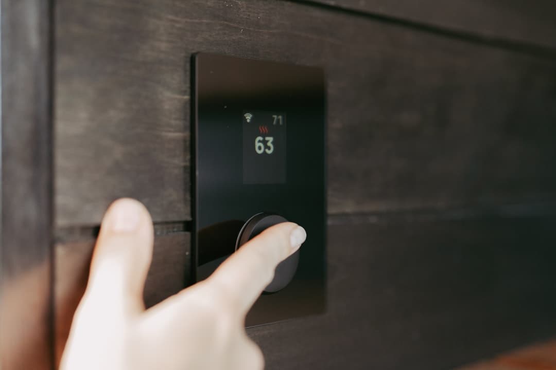 A hand adjusting a digital thermostat showing 63 degrees