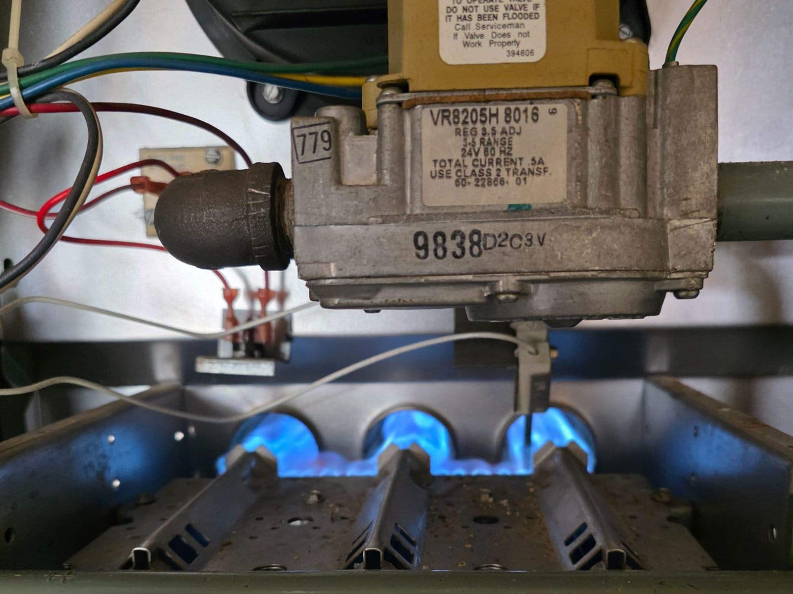 Gas furnace burners lit with blue flames beneath the gas valve