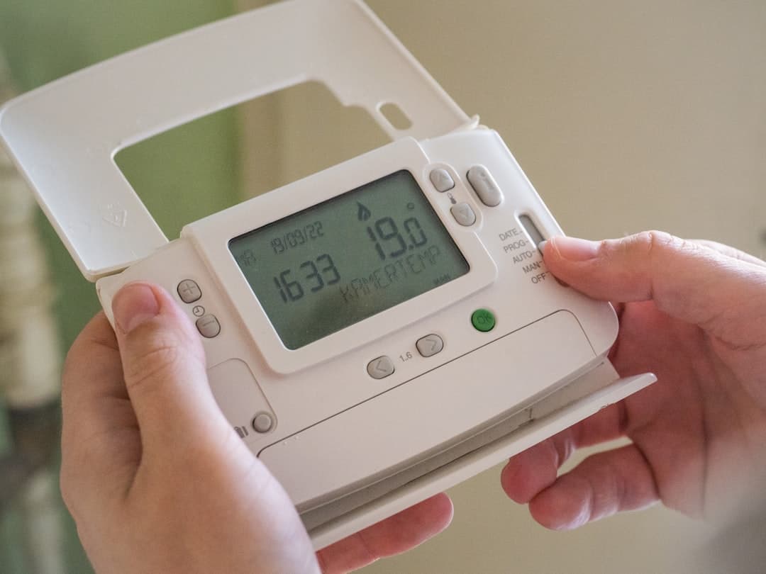 Hands holding a programmable thermostat and adjusting the temperature setting