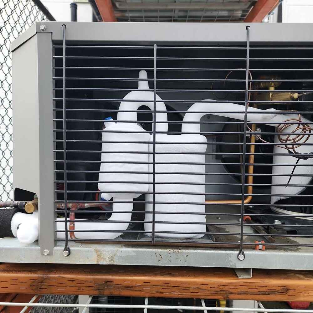 Frozen air conditioner coils and refrigerant lines inside an outdoor AC unit, showing visible ice buildup that indicates airflow or refrigerant issues.