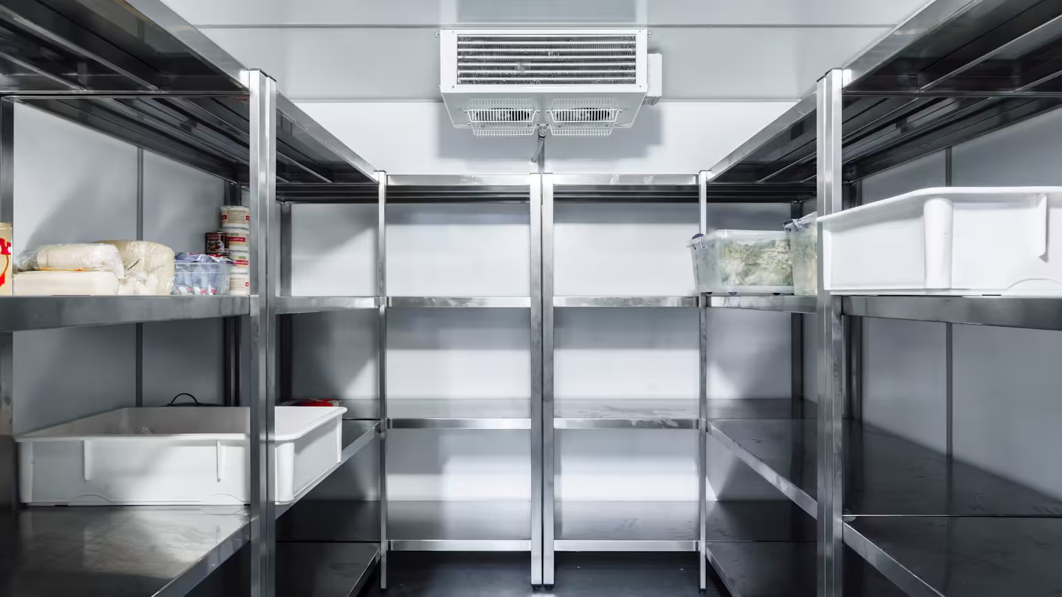 Commercial refrigeration systems maintenance shown in a walk-in cooler with stainless steel shelving and overhead cooling unit in a food storage facility.