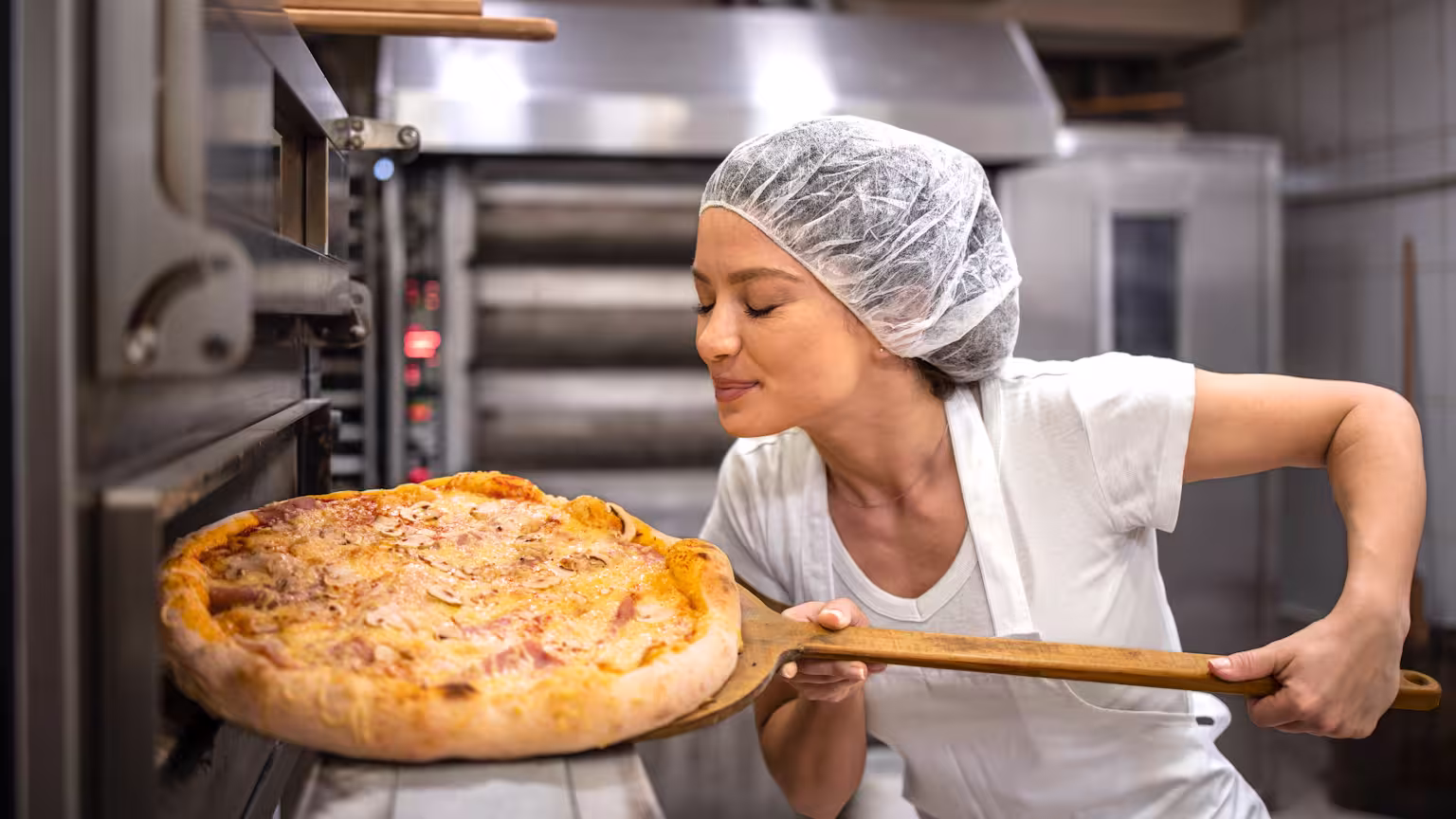 Pizza ovens service shown with a smiling chef pulling a freshly baked pizza from a commercial oven in a professional kitchen.